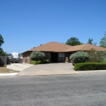 Single-story suburban house with a brown roof and driveway under a clear blue sky.