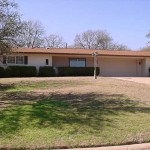 Single-story house with a beige exterior and a large front lawn.