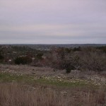 A vast landscape under a cloudy sky with sparse trees and grass.