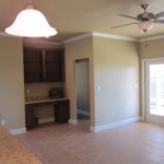 Empty beige living space with ceiling fan and built-in shelves.