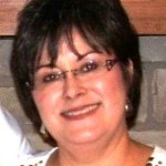 A smiling woman with glasses and short dark hair.