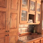 Rustic kitchen cabinets with glass doors and stone backsplash.