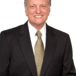 Smiling man in a suit and tie against a white background.