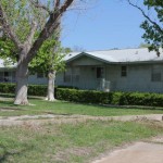 A single-story green house with a yard and trees.