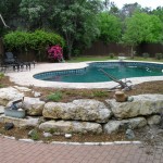Backyard pool with stone landscaping and trees.