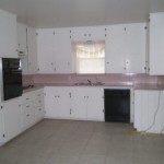 Empty white kitchen with pink countertops and black appliances.