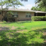 Single-story brick house with a green lawn and trees.