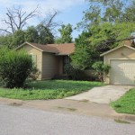 Single-story house with a driveway and green lawn surrounded by trees.