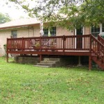 Wooden deck attached to a beige house with green lawn.