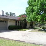 Suburban house with a large driveway and green trees.