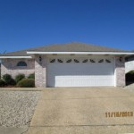 A suburban house with a white garage door and brick exterior under a clear blue sky.