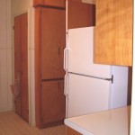 A wooden pantry cabinet next to a white refrigerator in a kitchen.