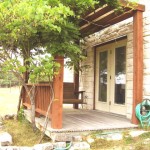 Rustic wooden porch with a tree and garden hose outside a building.