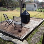 Two metal chairs and a chiminea on a stone patio in a backyard.