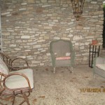 Cozy outdoor seating area with wicker chairs and a stone wall backdrop.