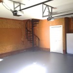 Empty garage with spiral staircase and closed door.